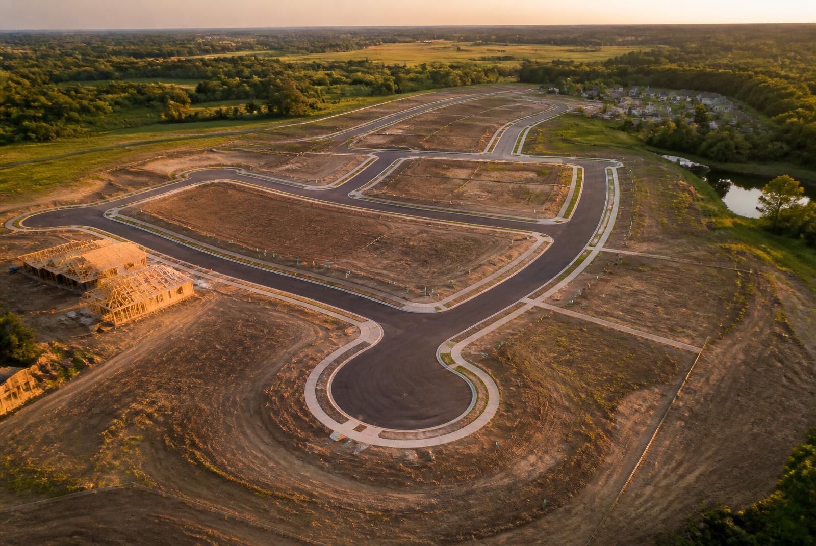 Aerial view of a new residential development with graded vacant lots and paved streets at golden hour
